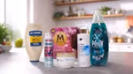 A variety of Unilever's Power Brands arranged on a kitchen counter. From left to right, you can see a bottle of Hellmann's Real Mayonnaise, a Degree deodorant spray labelled "WHOLE BODY DEO", a box of Magnum ice cream labelled "UTOPIA", a bottle of Dove body lotion pro-ceramides serum, a jar of Dove Intensive Repair cream and a bottle of Persil Wonder Wash. In the background, there's a modern kitchen with plants and various items on the shelves.